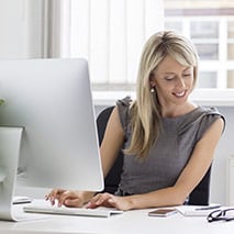 Woman looks at notes while typing on an iMac computer
